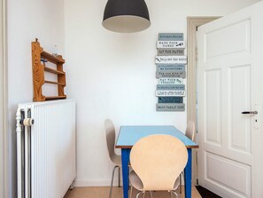 A small kitchen with a table and chairs, a radiator, a wooden shelf, and a wall with kitchen rules signs. - 4 Person Holiday Home in Skaerbaek (Skaerbaek)
