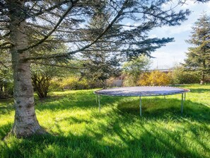 A trampoline in a grassy yard with trees and a house in the background.