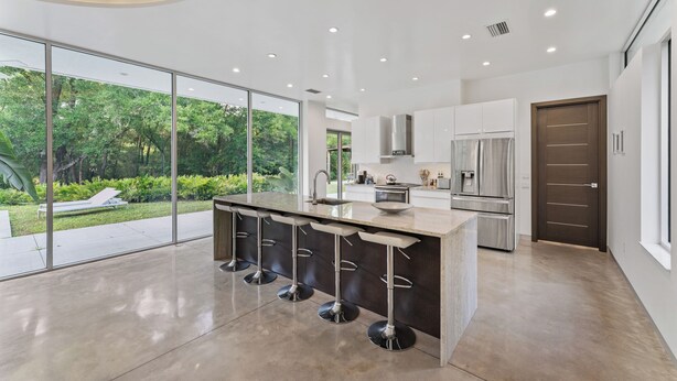 A modern kitchen with a central island, bar stools, and a view of a lush garden. - Floral City Oasis / Pool, BBQ Area & Forest View (Floral City)