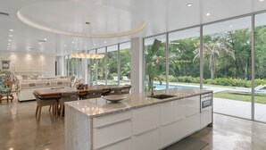 A modern kitchen with a large island, a dining area with wicker furniture, and a view of a swimming pool. - Floral City Oasis / Pool, BBQ Area & Forest View (Floral City)