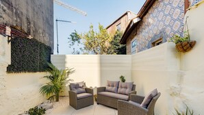 Un espace patio aménagé avec des meubles en osier, un mur blanc et une grue de construction en arrière-plan.