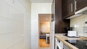 Une cuisine compacte avec des carreaux blancs, un lave-linge, une machine à café et un grille-pain.
