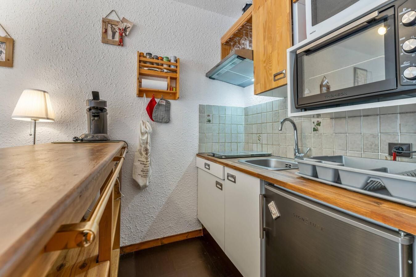 A compact kitchen with a wooden countertop, a built-in dishwasher, a microwave, and a sink.