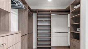 A walk-in closet with wooden shelving and drawers, featuring a hanging rack and a towel rack.