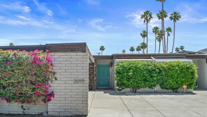 A residential property with a stone facade, a green door, and a well-maintained garden with pink flowers and green bushes.