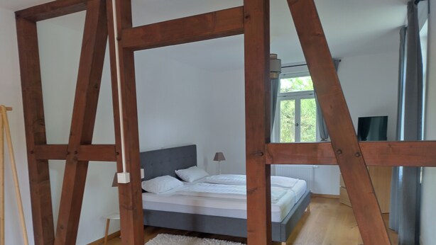 A bedroom with a bed, wooden beams, a window, and a radiator.