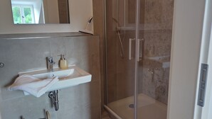 A modern bathroom with a glass-enclosed shower, a white sink with a soap dispenser, and a towel hanging on the wall.