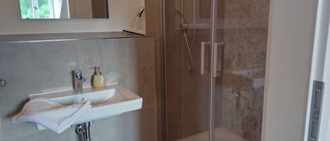 A modern bathroom with a glass-enclosed shower, a white sink with a soap dispenser, and a towel hanging on the wall.