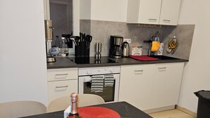 Une cuisine moderne avec des meubles blancs, un plan de travail noir et une table à manger agrémentée de sets de table rouges.