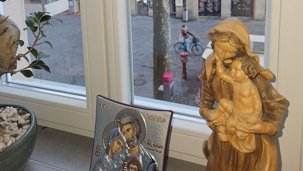 Une fenêtre donnant sur un arbre et des immeubles, une statue en bois et une icône encadrée.