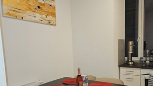 Un coin repas avec une table noire, quatre chaises beiges et des sets de table rouges. Une bouteille de vin est posée sur la table.