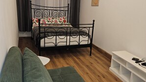 Une chambre à coucher avec un lit, un canapé vert, une table de chevet blanche et un plancher en bois.