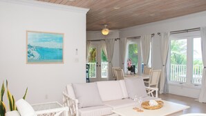 A spacious living area with a white sofa, a dining table, and a ceiling fan. - Tangerine Sunsets Pomelo East (Nassau Bahamas)