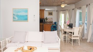 A cozy living room with a white sofa, a dining table with chairs, and a kitchen in the background. - Tangerine Sunsets Pomelo East (Nassau Bahamas)