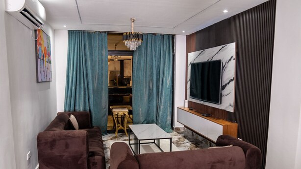 A modern living room with a sofa set, a TV mounted on the wall, and a chandelier. - Borelie Guest House  (Douala)