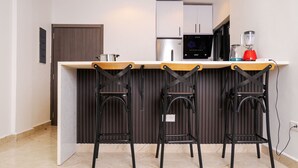 A compact kitchen with a countertop, a microwave, a blender, and three black chairs with a wooden top. - Borelie Guest House  (Douala)