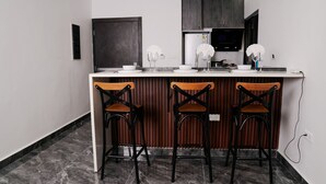A modern kitchen with a marble countertop, three bar stools, and a built-in stove. - Borelie Guest House  (Douala)