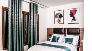 A bedroom with a bed, curtains, and two framed artworks on the wall. - Borelie Guest House  (Douala)