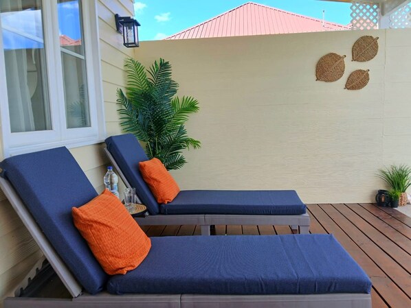 Two lounge chairs with blue cushions and orange pillows, a potted plant, and decorative wall art.