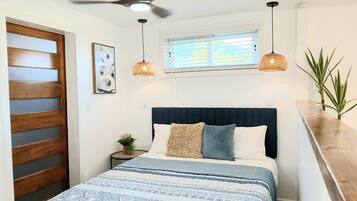 Een slaapkamer met een bed, een plafondventilator, een raam met zonwering en een kamerplant.