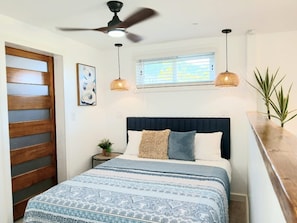Ein Schlafzimmer mit einem Bett, einem Deckenventilator, einem Fenster mit Jalousien und einer Zimmerpflanze.