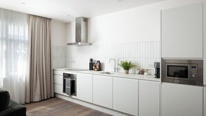 A modern kitchen with white cabinetry, a stainless steel range hood, a built-in oven, and a microwave. - Urban Rest Dublin Central (Dublin)