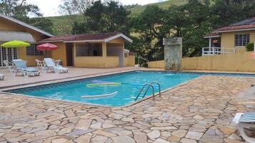 Una piscina con baldosas de piedra, sillas de descanso y sombrillas.