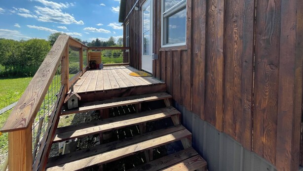 A wooden staircase leading to a deck with a metal railing, surrounded by a wooden fence and potted plants. - Quiet 2-bedroom country cabin with scenic views 3 miles from Norwich NY. (Norwich)