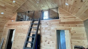 A wooden cabin interior with a central staircase, a ceiling fan, and a window on the upper level. - Quiet 2-bedroom country cabin with scenic views 3 miles from Norwich NY. (Norwich)