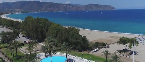 A resort with a large swimming pool, beach access, and mountainous views.