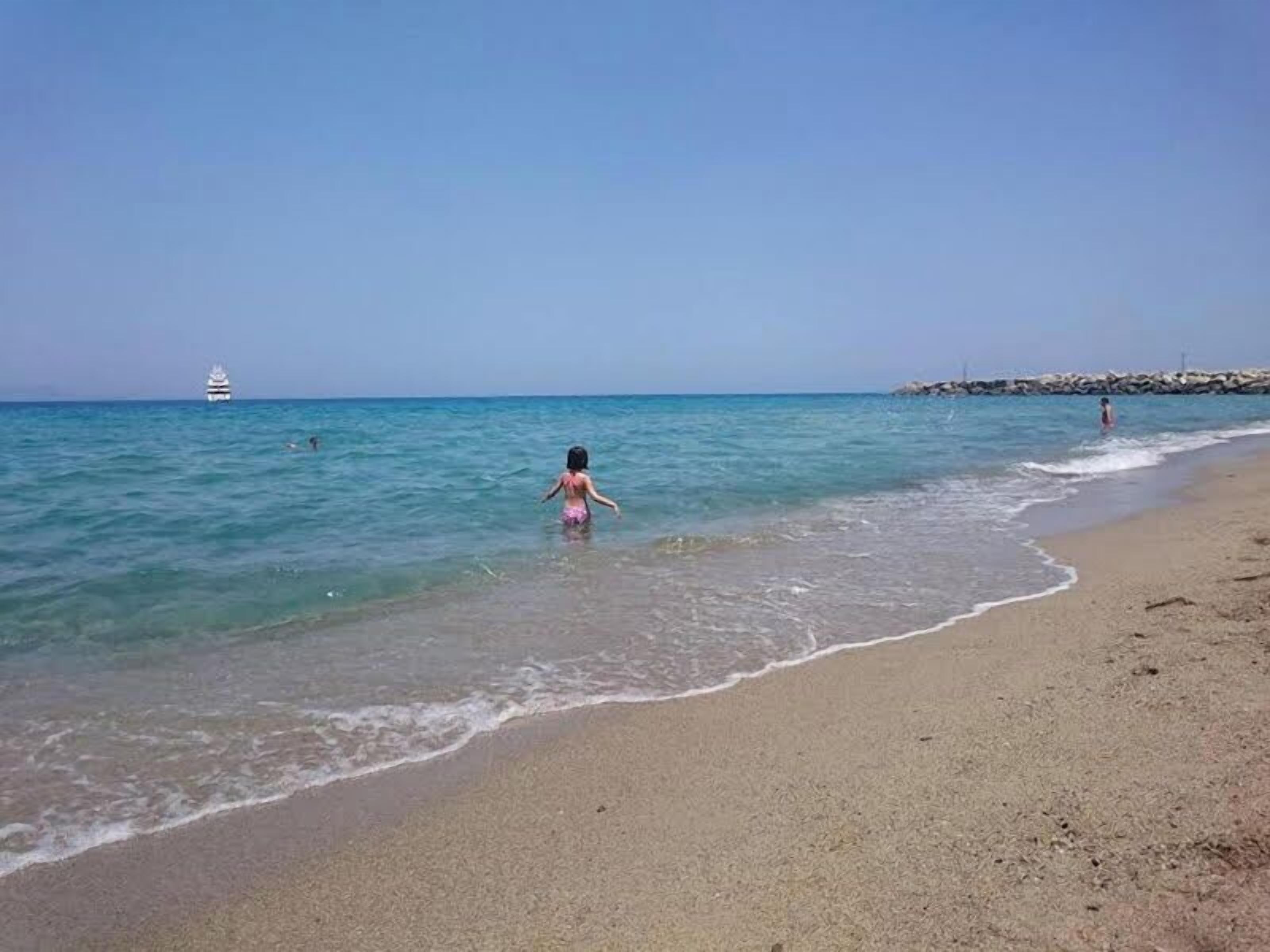 A beach with clear water, a distant boat, and a rocky breakwater.