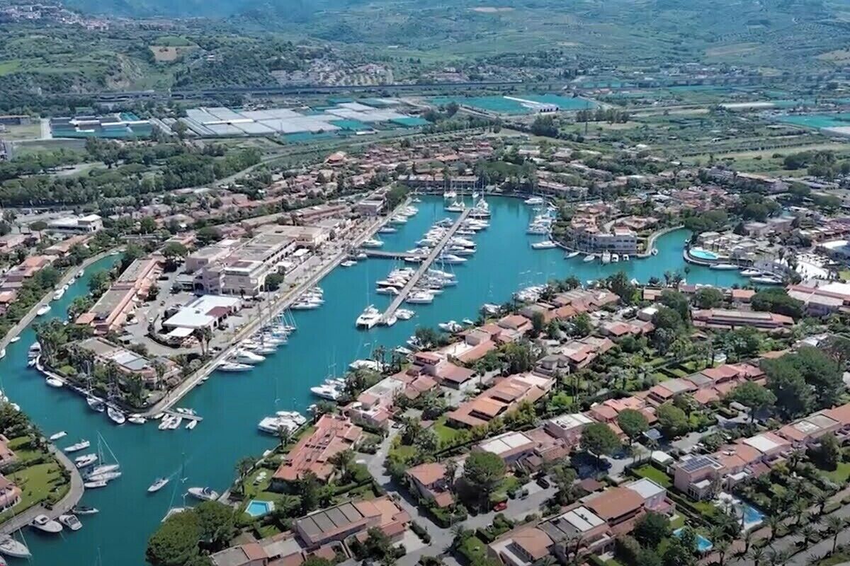 Vista aérea de un puerto deportivo con numerosas embarcaciones amarradas, rodeado de edificios residenciales y zonas verdes.