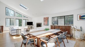 A spacious living room with a large wooden dining table, white sofas, and a fireplace.