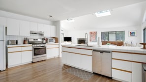 A modern kitchen with white cabinetry, stainless steel appliances, and a wooden floor.