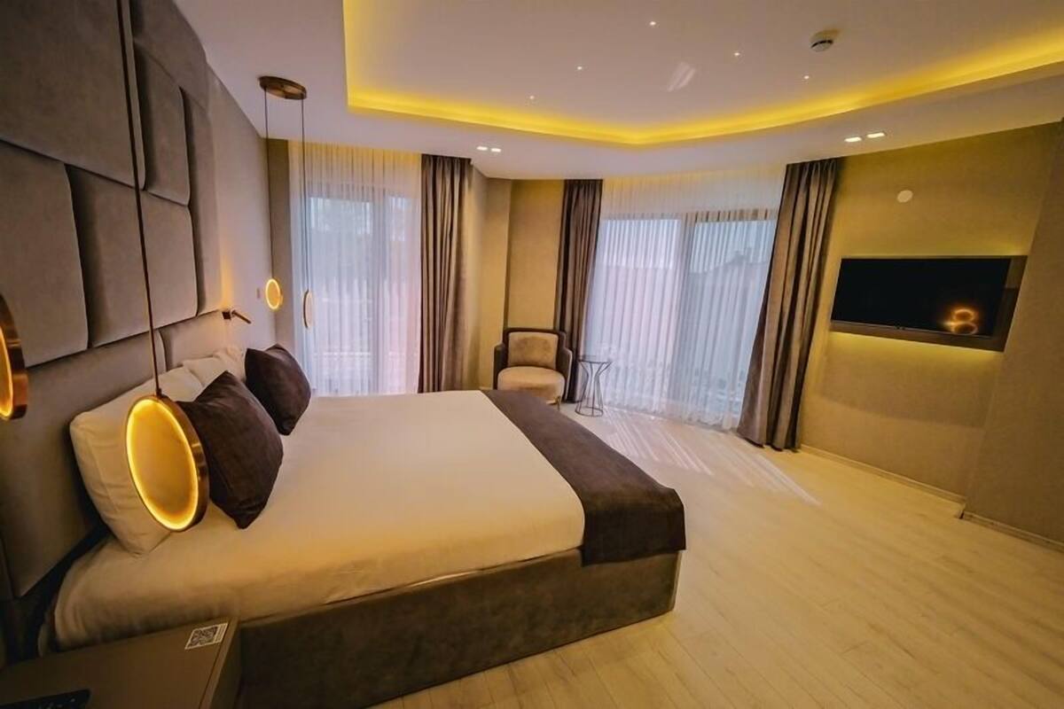 A modern bedroom with a large bed, a TV mounted on the wall, and a small table.