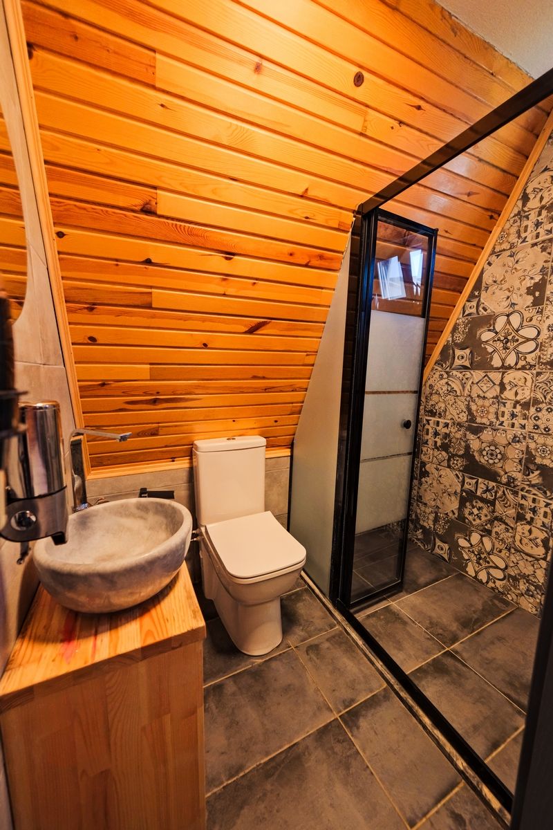 Et lille badeværelse med træpaneler, toilet, vask og bruseområde.