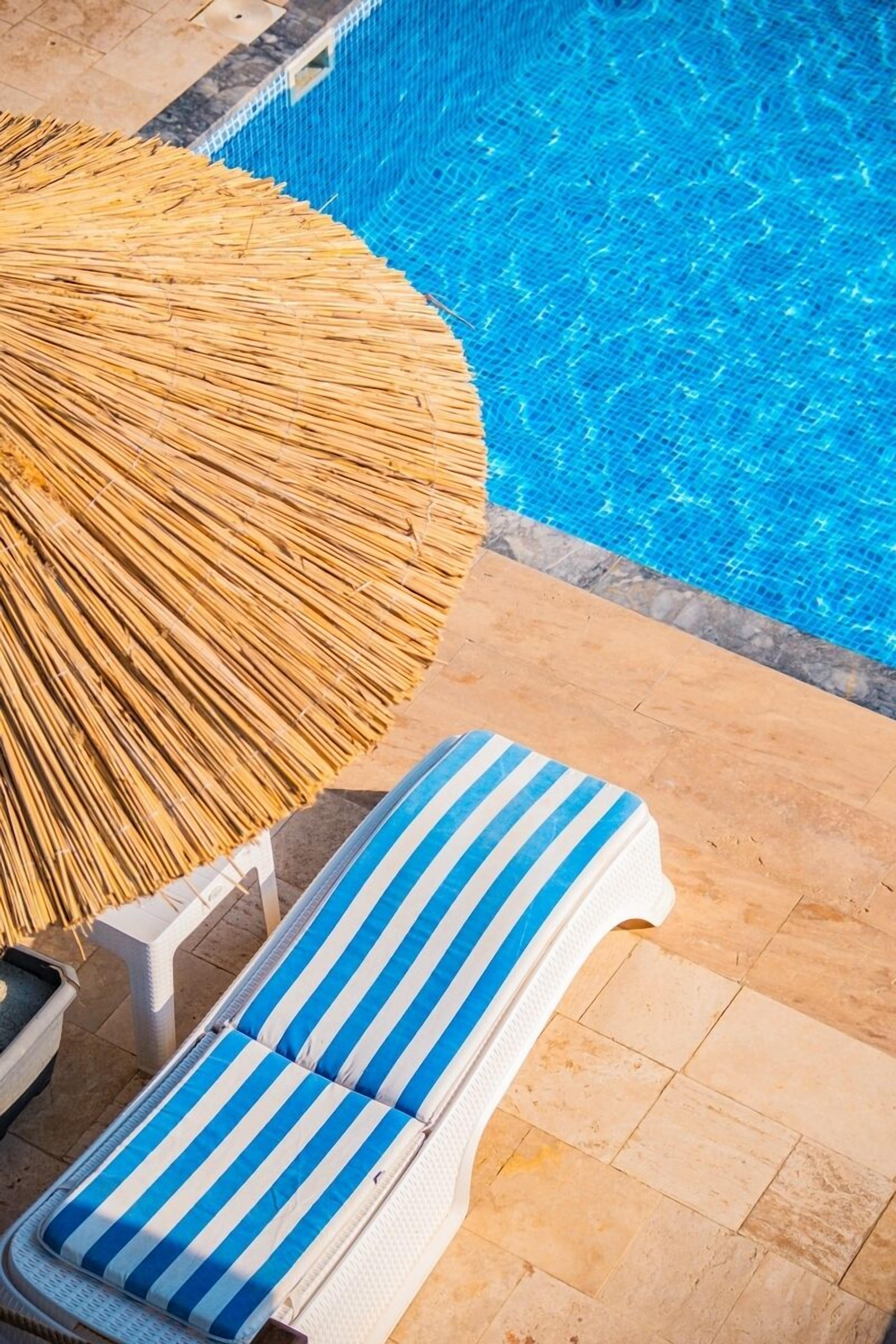 A poolside area with a lounge chair and a straw umbrella.