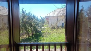 A view through a window with a metal railing, a clear sky, and a green landscape with trees and a building in the background. - Nice studio in the heart of Le Monêtier-les-Bains (Le Monêtier-les-Bains)