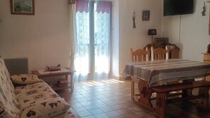 A cozy living room with a patterned sofa, a wooden dining table, and a green floor lamp. - Nice studio in the heart of Le Monêtier-les-Bains (Le Monêtier-les-Bains)