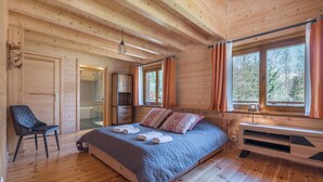 Un dormitorio de cabaña de madera con cama, una silla, un escritorio y una ventana con cortinas.
