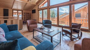 Un salón amplio con un gran techo de madera, un sofá, una mesa de centro y vistas a las montañas a través de grandes ventanales.