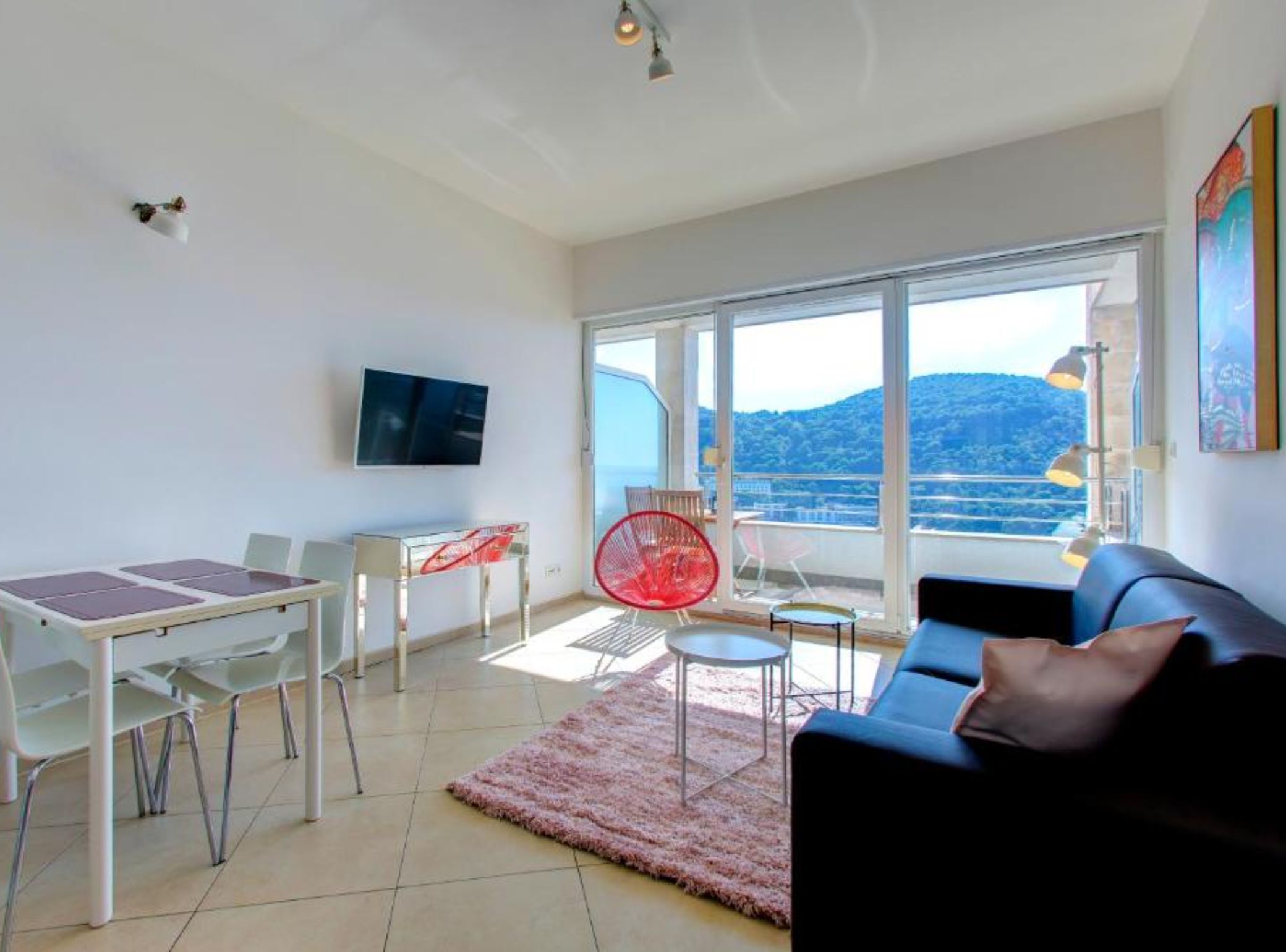 Een moderne woonkamer met een groot raam, een televisie, een eethoek en een bank.