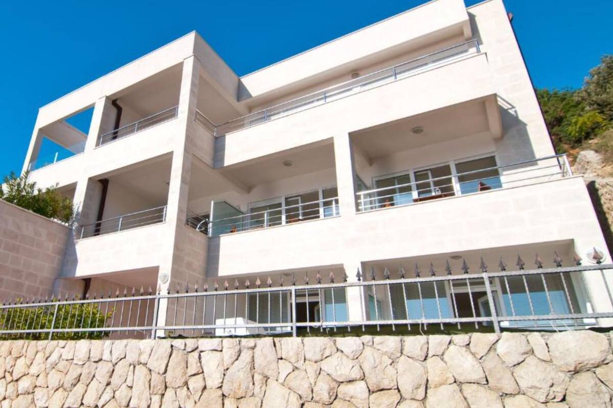 A modern multi-story building with balconies and a stone wall in the foreground.