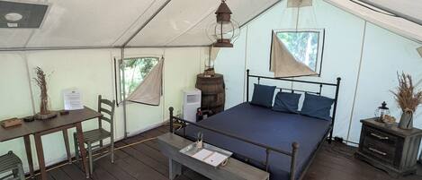 A tented room with a bed, a table, a chair, and a bench.