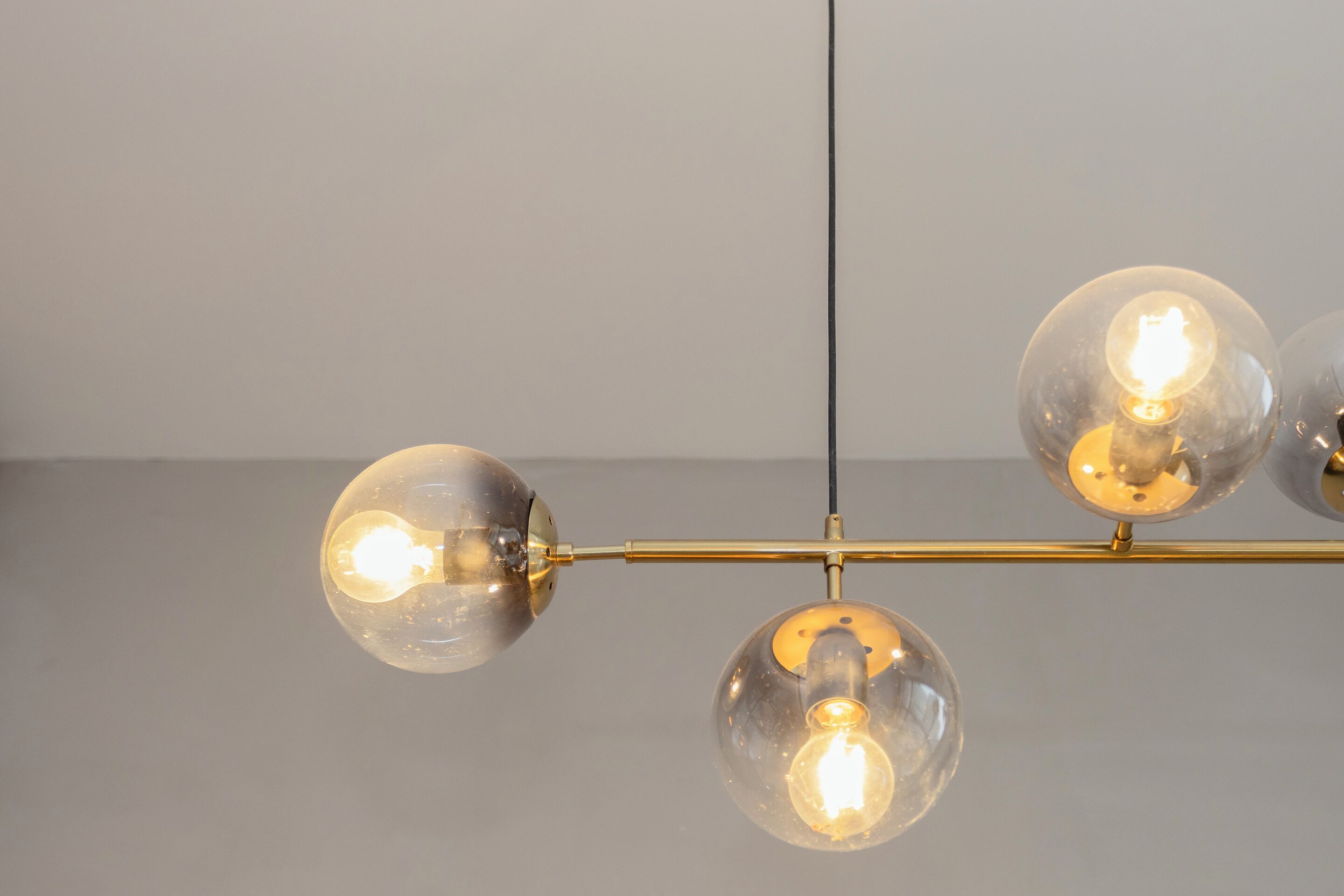 Un lustre composé de trois globes en verre sphériques et d’une tige en métal de couleur or.