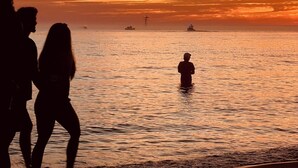 Ein Sonnenuntergang über einem ruhigen Meer mit Silhouetten von Personen und einem Boot.