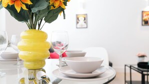 Una mesa de comedor con un jarrón amarillo, una copa de vino y vajilla blanca.