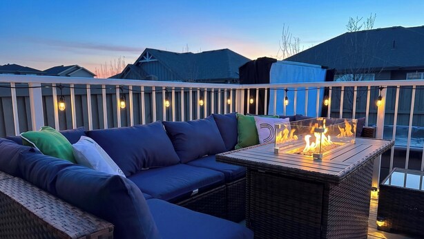 A balcony with a sofa, a table with a fire feature, and string lights.