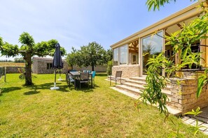 A house with a stone exterior, a glass door, and a small patio with a table and chairs. - Gîte Refuge des Amis  en Vendée de 300m² (Chanverrie)