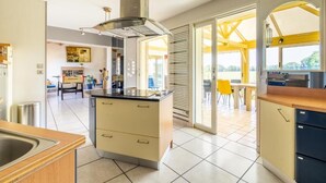 A modern kitchen with a central island, a built-in stove, and a large window overlooking a deck. - Gîte Refuge des Amis  en Vendée de 300m² (Chanverrie)